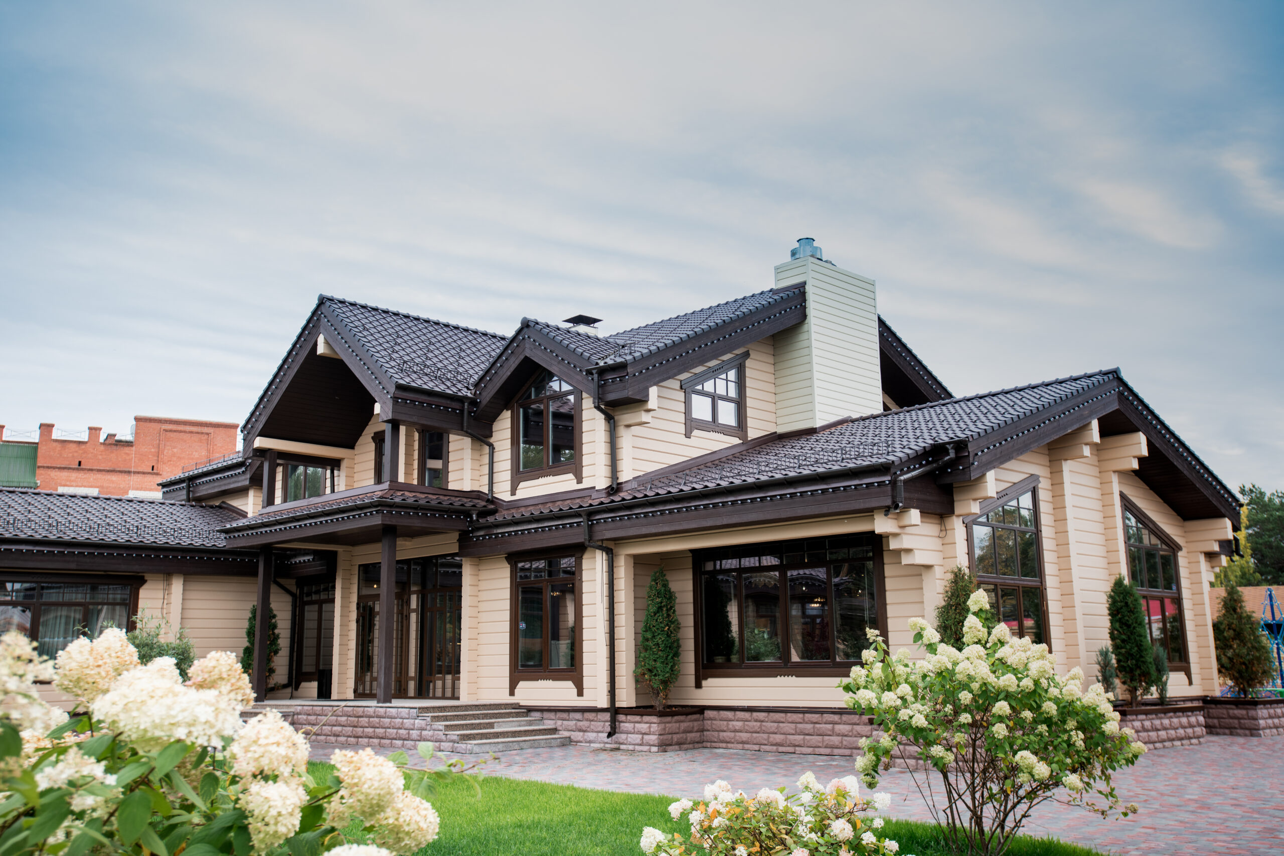 View of luxurious modern house with decorative elements around windows and front yard with blooming white flowers